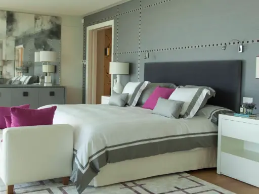 Ideas para diseñar tu habitacion: cama moderna con detalles grises y rosas, mesitas blancas, sofá y espejo decorativo.