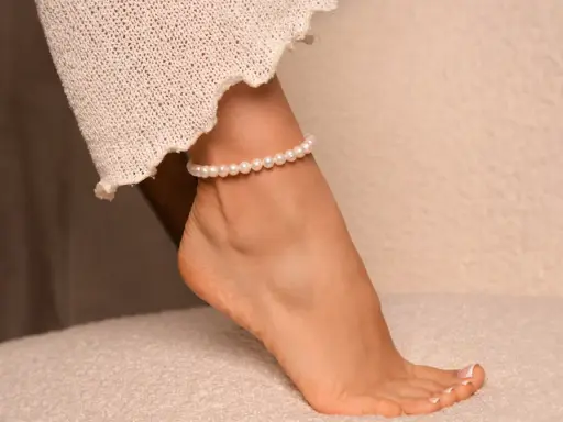 Delikatna bransoletka z pereł na prawej nodze, ozdobiona koronkową tkaniną, dodaje elegancji.