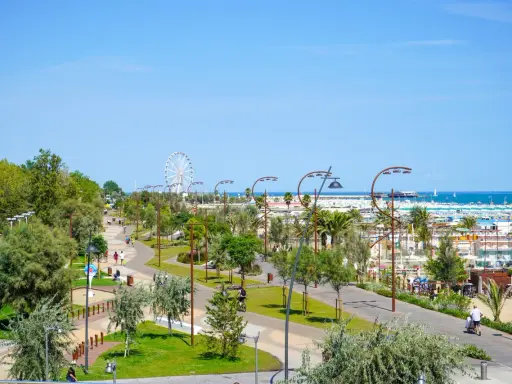 Passeggiata nel verde del parco del mare Rimini, con gente che cammina e pedala, e la ruota panoramica sullo sfondo.