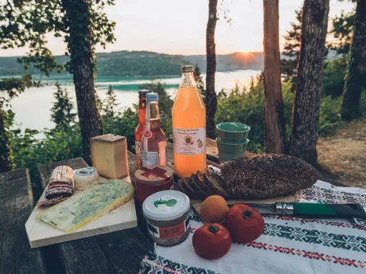 Pique-nique avec fromages, pain de campagne, jus de poire et terrine, un aperçu des spécialités culinaires Jura au bord d'un lac.