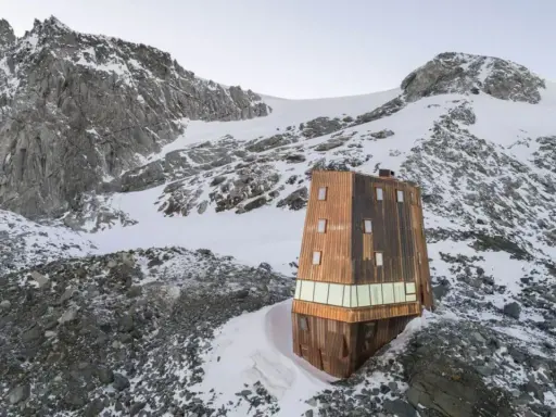 Il rifugio Sasso Nero, un'architettura moderna in legno, si erge solitario tra rocce e neve, dominato da imponenti vette montuose.