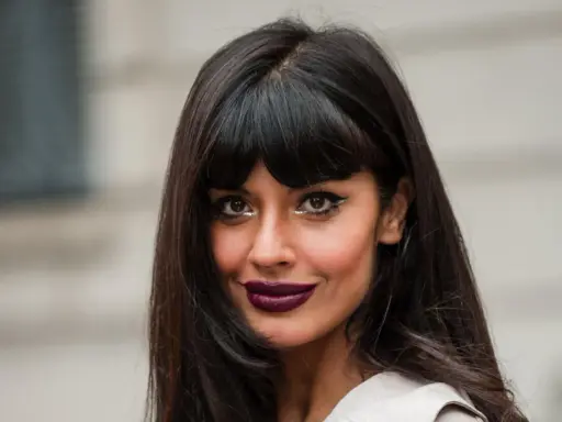 Frau mit leichter Pony und langen, dunklen Haaren, auffälligem Make-up und dunklem Lippenstift.