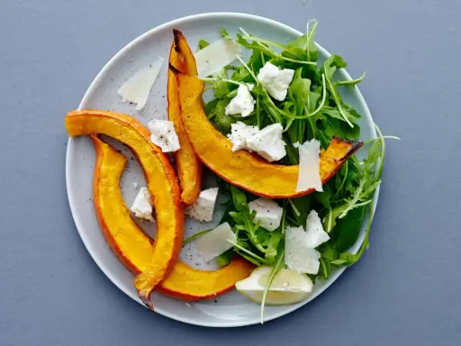 En härlig sallad med ruccola och fetaost, toppad med ugnsrostad pumpa och en citronskiva.