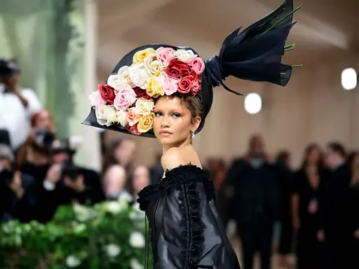Zendaya stuns at the Met Gala in a dramatic black gown and a voluminous hat adorned with a cascade of colorful roses.