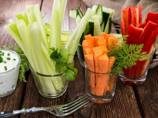Geschnittene Karotten, Sellerie, Gurken und Paprika in Gläsern, dazu ein Dip. Perfekte Snacks nach dem Sport für gesunde Erholung.
