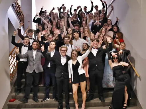 Schüler feiern Mottowoche Filme und Serien auf einer Treppe, alle in schicken Outfits, viele mit V-Gesten.