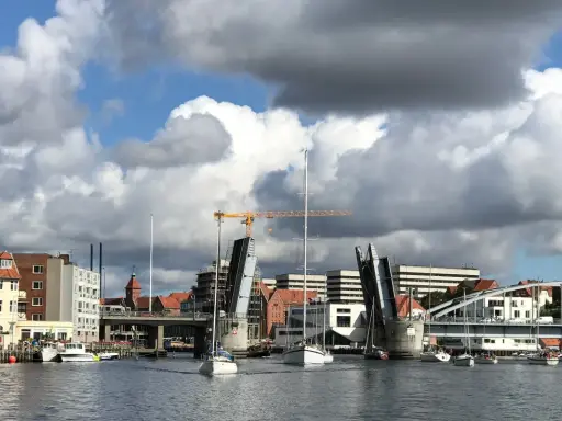 Sonderborg Hafen mit geöffneter Klappbrücke, Segelbooten und Gebäuden unter dramatischem Wolkenhimmel.