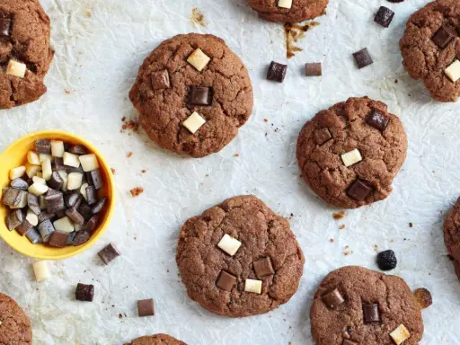 Gros plan sur des cookies au chocolat parsemés de morceaux de chocolat blanc et noir. Un petit bol jaune contient des morceaux de chocolat, comme un cookie stick.