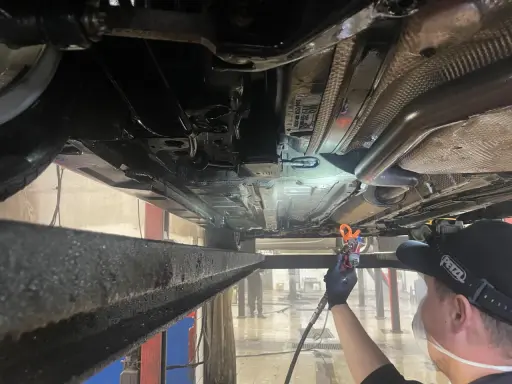 Profesjonalne zabezpieczenie antykorozyjne podwozia samochodu. Mechanik aplikuje preparat ochronny.