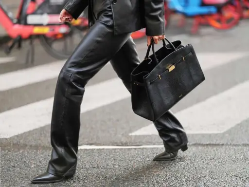 A person walks across a crosswalk in a chic leather pants outfit, perfect for winter. They carry a stylish black handbag.