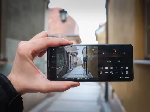 Dłoń trzyma smartfon Sony Xperia Pro i, kadrując wąską uliczkę. Widoczne ustawienia aparatu.