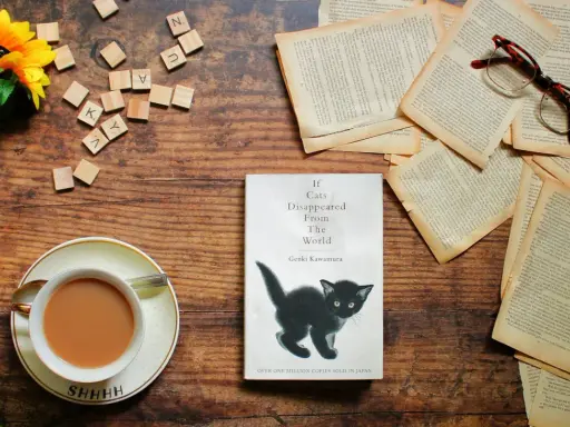 Libro "If Cats Disappeared From The World" con un gattino nero, occhiali, fiori e una tazza di tè. La trama esplora un mondo senza gatti.