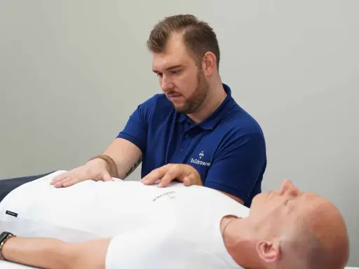 Terapeuta wykonuje zabieg z zakresu osteopatii wisceralnej, delikatnie dotykając brzucha pacjenta.