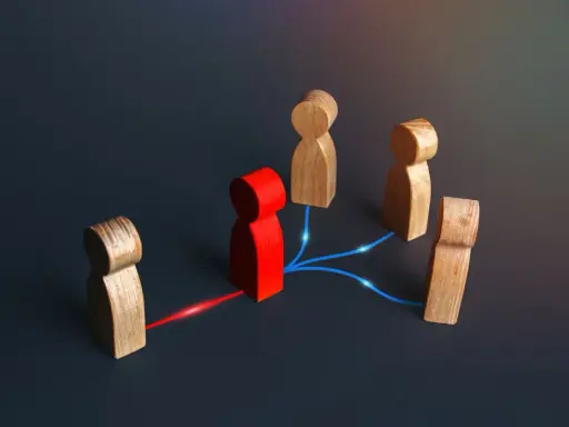 Figuras de madera conectadas por líneas de luz. Una figura roja central actúa como nodo, conectando a otras figuras, representando el papel de intermediarios financieros.