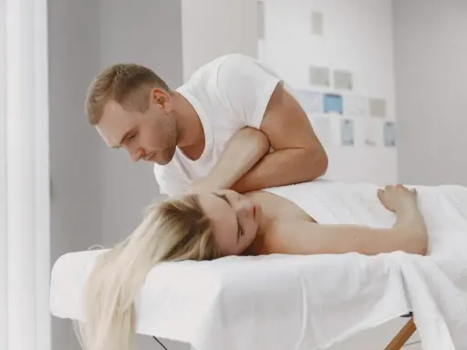 Fizjoterapeuta wykonuje neuromobilizację nerwu promieniowego u pacjentki leżącej na kozetce.