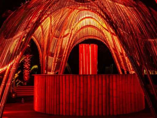 Struttura in bambù illuminata di rosso, con un bancone e un'installazione luminosa centrale. Atmosfera da house techno.