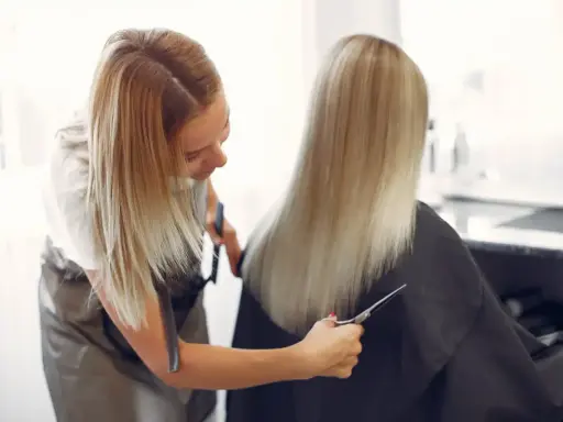 Peluquera con tijeras realiza un corte de cabello en v a una clienta con cabello rubio largo.
