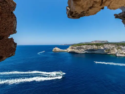 Blick durch Felsformationen auf das tiefblaue Meer bei Bonifacio, Korsika. Boote gleiten über die Wellen.