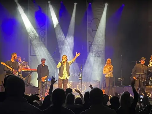 Medlemmar av Dr Hook uppträder på scenen under en konsert, med sångaren i centrum som sjunger i mikrofonen.