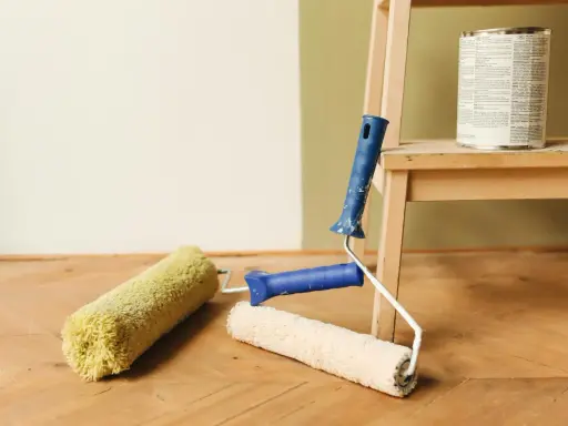 Färgburk och roller på trägolv, redo att måla på tapet.