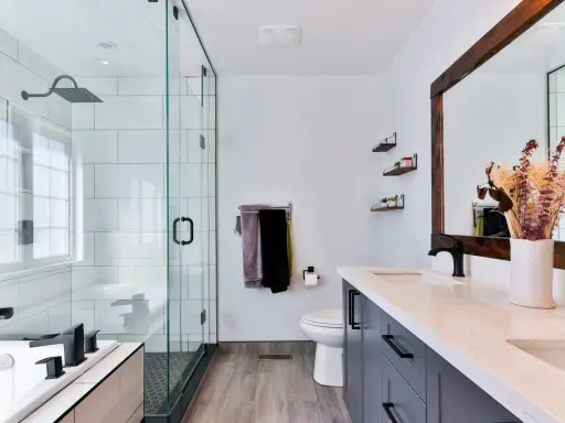Baño moderno con ducha de cristal, inodoro, lavabo doble y un gran espejo. Las ventanas para baños pequeños son clave para la luminosidad.