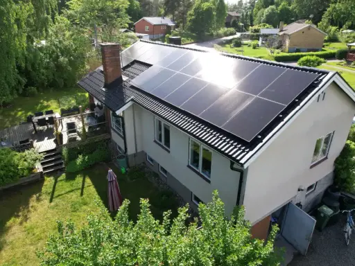 Ett hus med solpaneler på taket, redo att fånga solens energi. En grönskande trädgård och en altan inbjuder till avkoppling.