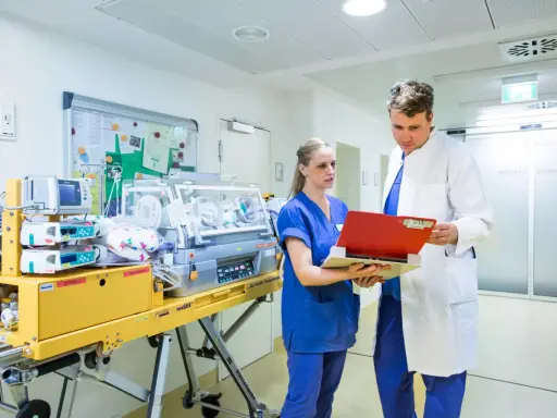 Personale medico discute in terapia intensiva neonatale accanto a un'incubatrice.