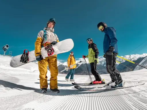 Grupa narciarzy i snowboardzistów na ośnieżonym stoku z widokiem na góry.
