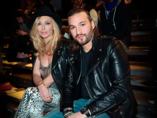 Steve Angello fru, Isabella, med sin blonda frisyr och hatt, sitter bredvid honom. Båda bär svarta läderjackor.