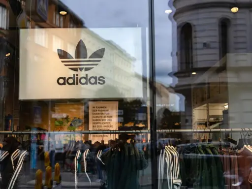 Witryna sklepu z logo adidas, marki pochodzącej z Niemiec. Wieszaki z ubraniami, w tym kurtki i bluzy z charakterystycznymi trzema paskami.