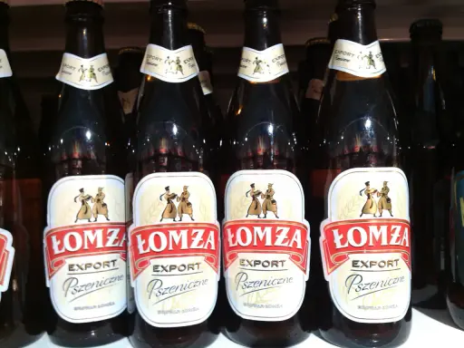 Butelki piwa Łomża Export Pszeniczne w rzędzie. Etykiety z postaciami i kłosem zboża.