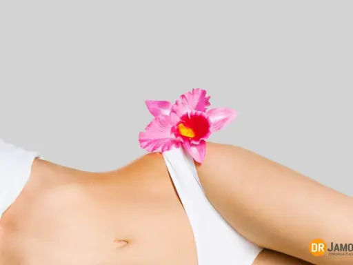 Delikatna różowa orchidea na tle kobiecego ciała, symbolizująca naturalne piękno i różnorodne rodzaje warg sromowych.