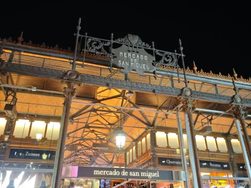 Das Mercado de San Miguel bei Nacht, mit seinem verzierten Eingang und den Lichtern, die durch das Glasdach scheinen.