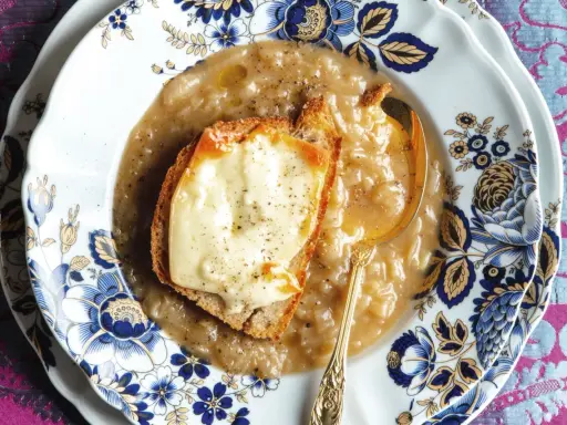 Piatto di zuppa di cipolle fumante, con crostino di pane e formaggio fuso, servita su un elegante piatto decorato.
