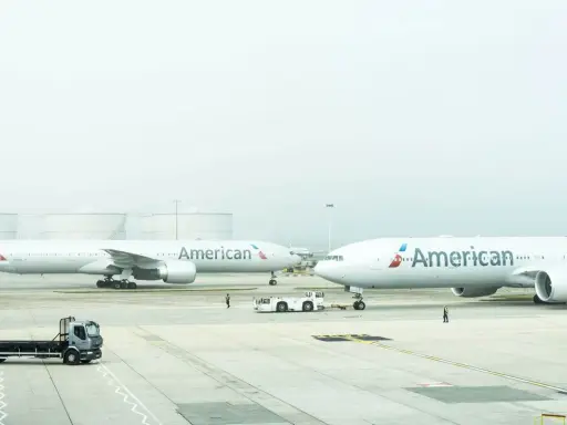 Dwa samoloty American Airlines na płycie lotniska, gotowe do przyjęcia bagażu rejestrowanego.