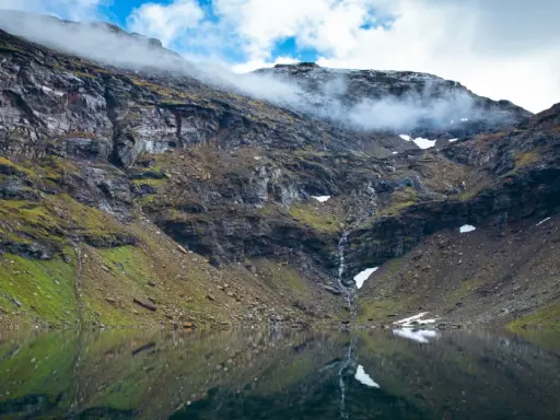 Vacker fjällsjö med en porlande vattenfall, perfekt för dagsturer i Abisko. Moln sveper över bergstopparna.