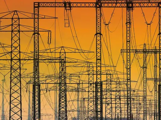 Silhouetten von Strommasten und Leitungen vor einem orangen Himmel. Ein Netz von **Polen Strom** erstreckt sich in die Ferne.