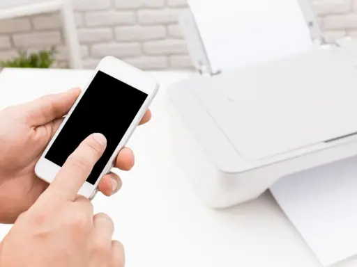 Instrukcja: jak połączyć telefon z drukarką. Smartfon w dłoni, obok drukarka z papierem.