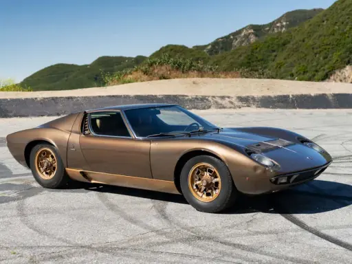 Ein brauner Lamborghini Miura S steht auf einer asphaltierten Straße mit Bergkulisse.