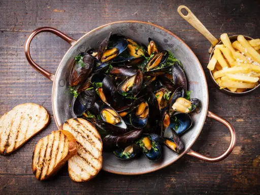 Moules marinières, une spécialité culinaire normande, servies dans une marmite en cuivre avec des frites et du pain grillé.
