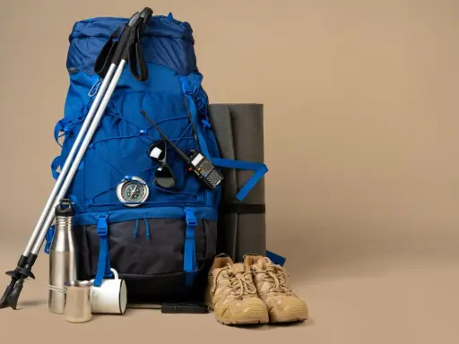 Niebieski plecak trekkingowy, kije, buty, mata, kompas, krótkofalówka i termos – wszystko gotowe na wyprawę.