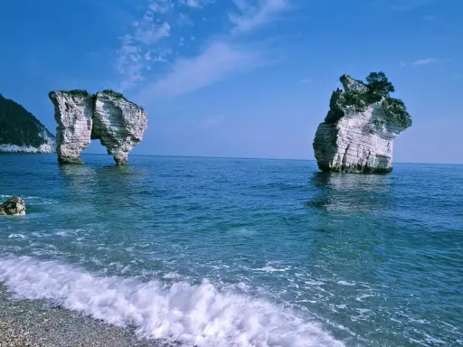 La **Baia delle Zagare** con le sue iconiche faraglioni bianchi che emergono dal mare blu intenso, sotto un cielo limpido.