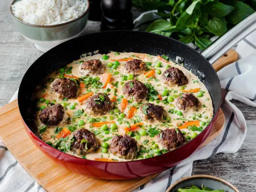 Herzhafte Fleischbällchen in cremiger Sauce mit Erbsen und Karotten, ein köstliches Wikingertopf Rezept, serviert in einer roten Pfanne.