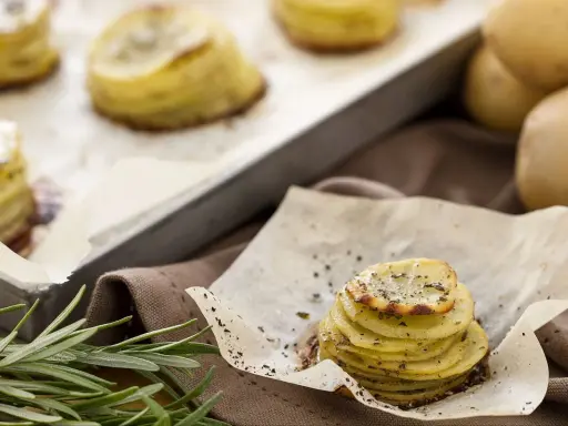 Tourte de pommes de terre fines et dorées, assaisonnée d'herbes, sur du papier sulfurisé.
