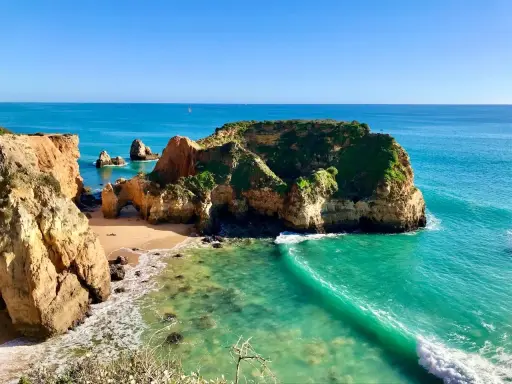 Traumhafte Felsformationen und türkisfarbenes Wasser am Praia de Alvor. Eine kleine Bucht mit Sand und grünen Klippen.