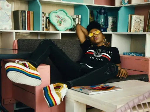 Une jeune femme aux lunettes rondes dorées se détend sur un canapé, ses chaussures arc-en-ciel colorées bien en évidence. Elle incarne le parfait "chill traduction".