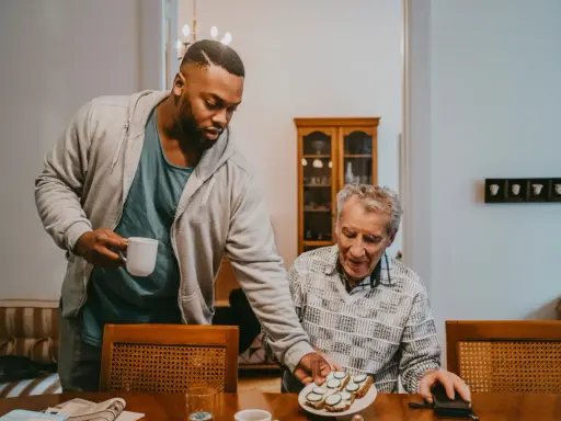 Un jeune homme sert une tasse à un aîné, partageant un moment de **colocation intergénérationnelle** autour d'un plateau de tartines.