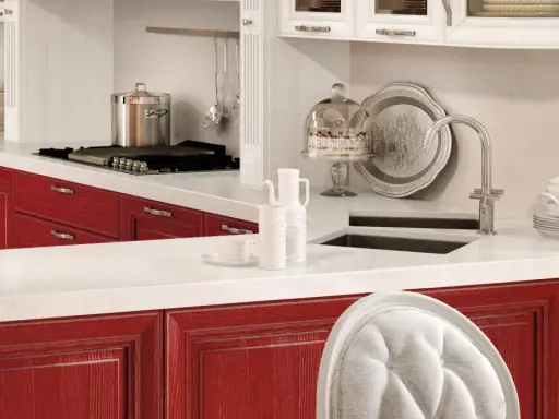 Cucina con ante rosse, piano bianco, pentola sul fornello, torta sotto campana di vetro. Okite cos'è? Un piano di lavoro resistente e bello.