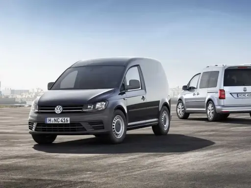 Dos furgonetas Volkswagen Caddy, una negra y otra plateada, demuestran su versatilidad como vehículo mixto adaptable en un entorno portuario.