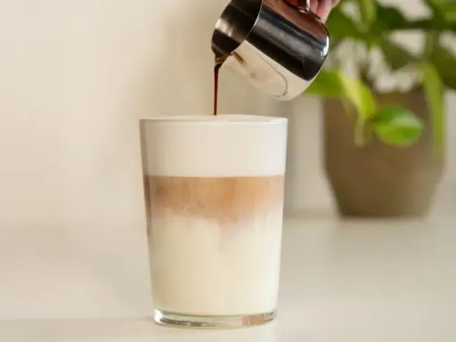 Espresso wird in ein Glas mit Milch und Milchschaum gegossen. Ein perfektes Latte Macchiato Rezept.